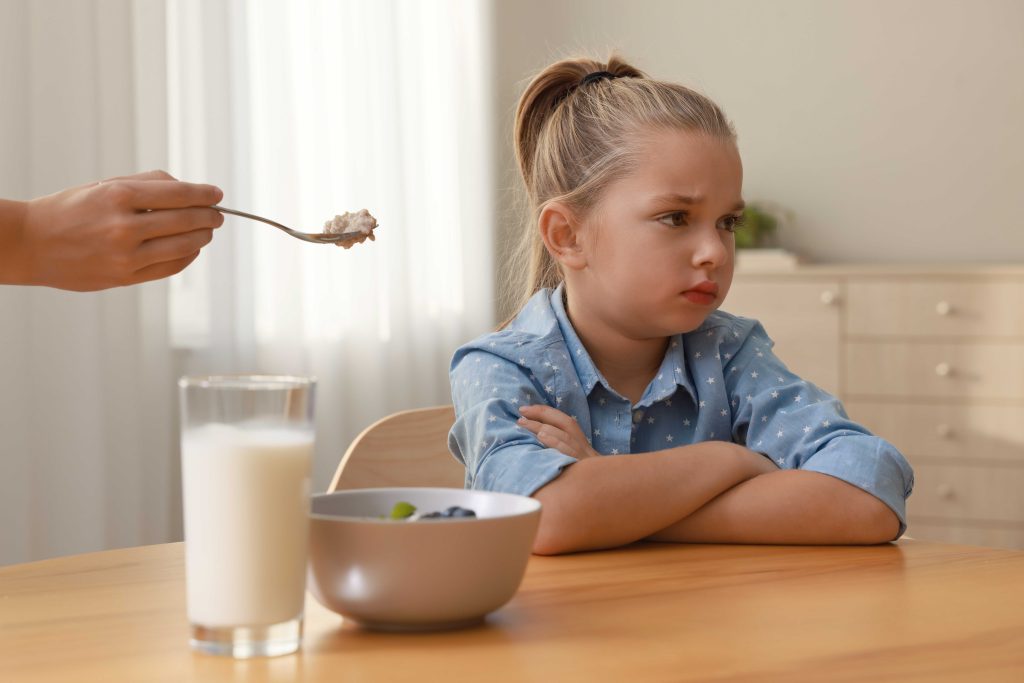 girl sitting at wooden table refusing to eat food